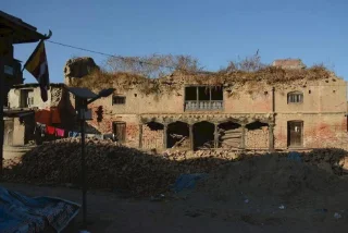 Dilapidated two-story brick building with a crumbling facade, overgrown with vegetation and piles of rubble.