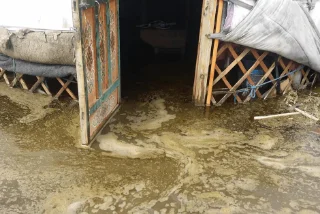 Floodwater entering a yurt in a muddy rural area.