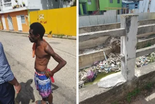 A man stands on a sunny street with a yellow wall behind him. He faces another person partially visible. Beside, a drainage area is filled with trash, showing urban neglect. The mood is concerned.