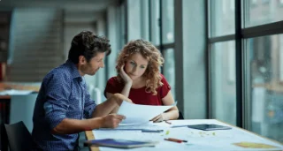 A man and woman at a table, examining papers intently