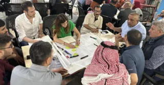 Community workshop with participants collaborating around a table using notes and markers.