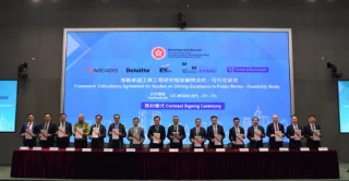 Formal contract signing ceremony with representatives from Arcadis, Deloitte, EY, Mott MacDonald, KPMG, and Turner & Townsend, alongside the Hong Kong Development Bureau. Participants hold signed documents in front of a large digital display showing consultancy logos and bilingual text announcing the Framework Consultancy Agreement for feasibility studies on public works excellence.