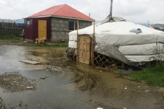 Yurt and house in muddy flood-prone rural area.