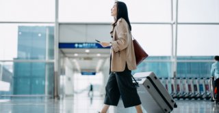 Traveler with luggage using smartphone inside airport terminal.