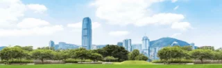 Skyline view of a city with modern skyscrapers under a blue sky. Foreground features a lush green park with trees, creating a serene contrast.