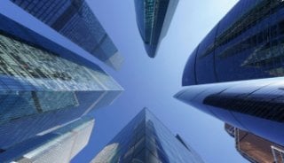 View from the ground looking up at modern glass skyscrapers against a clear blue sky