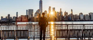 Person viewing city skyline at sunset from waterfront.