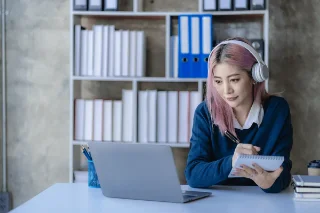 A woman with pink hair wearing headphones, sitting at a desk
