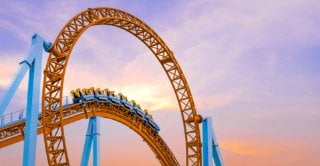 Roller coaster train navigating a bright orange loop and curved track against a colorful sunset sky.